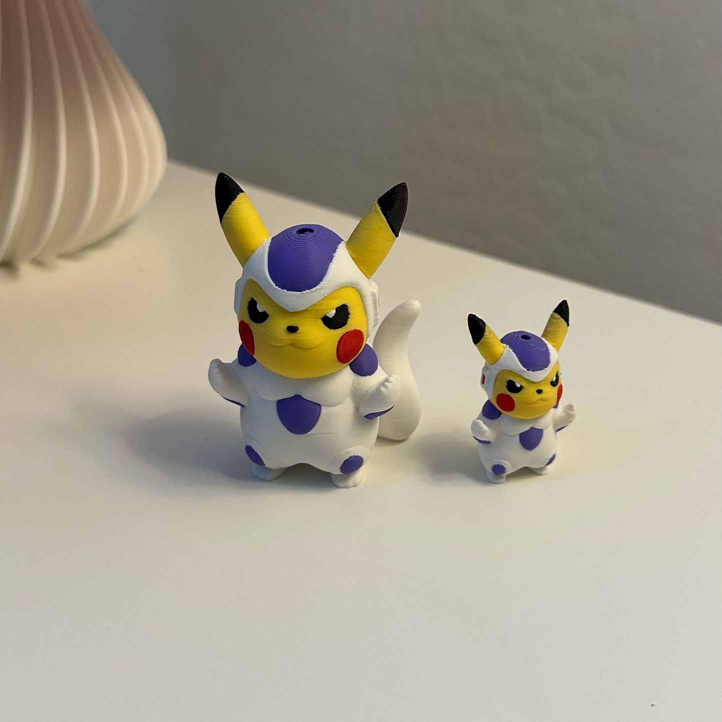 Two small figurines resembling Pikachu on a white surface with a red lampshade in the background.